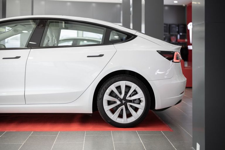 A modern white electric car showcased on a red carpet inside a showroom.