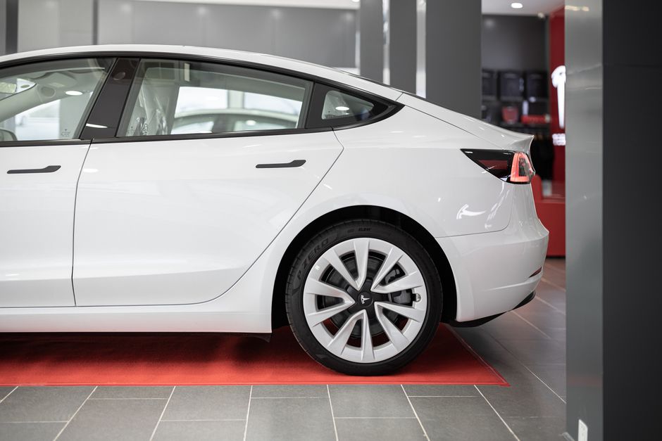 A modern white electric car showcased on a red carpet inside a showroom.
