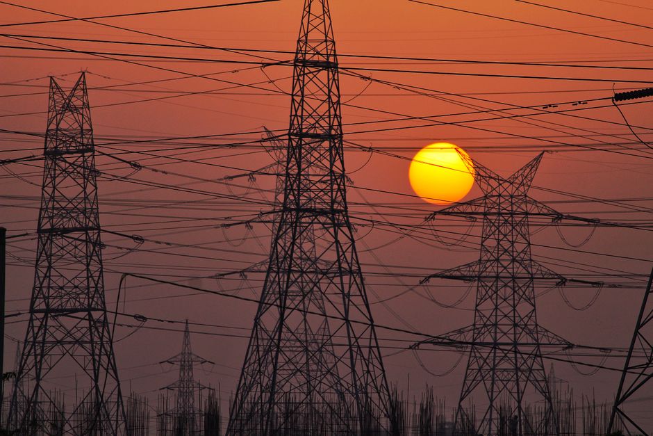 High-tension power lines silhouetted by a dramatic and colorful sunset sky, representing energy distribution.