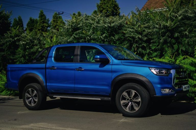 A blue pickup truck parked on a sunny day in Kyiv, Ukraine, surrounded by lush greenery.