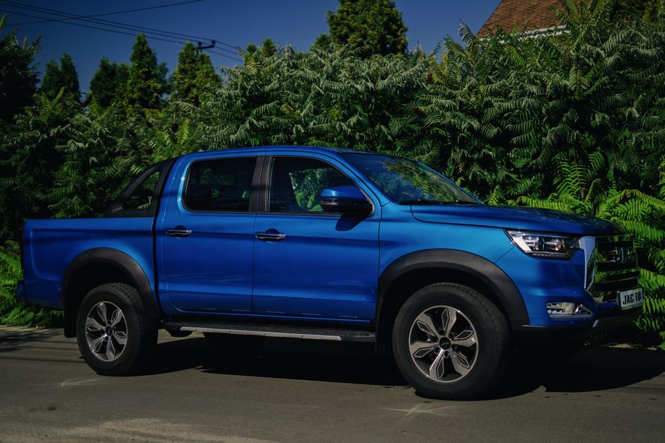 A blue pickup truck parked on a sunny day in Kyiv, Ukraine, surrounded by lush greenery.