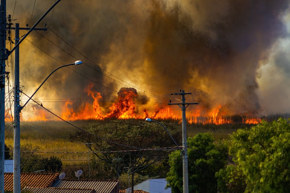 A blazing wildfire spreads through a field, emitting thick smoke.