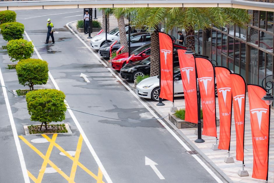 Aerial view of multiple Tesla cars parked alongside branded flags in a city street.