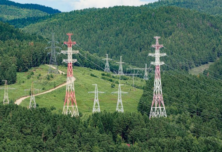High voltage transmission towers stretching through lush green forest hills, showcasing energy infrastructure.