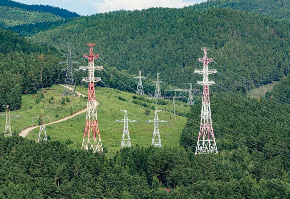 High voltage transmission towers stretching through lush green forest hills, showcasing energy infrastructure.