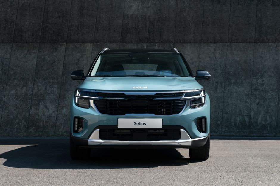A modern blue Kia Seltos SUV parked against a concrete wall in daylight.