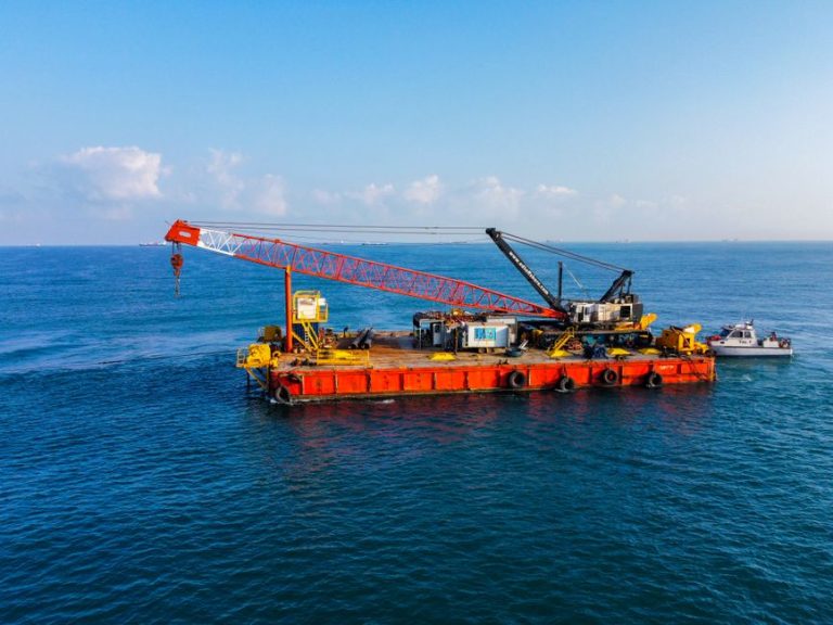 A large barge equipped with heavy cranes floating on the ocean on a clear day.