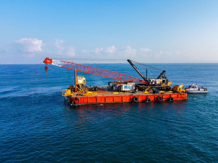 A large barge equipped with heavy cranes floating on the ocean on a clear day.