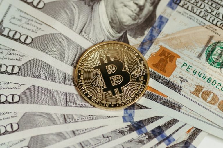 A Bitcoin coin placed on a stack of hundred dollar bills, symbolizing cryptocurrency and traditional wealth.