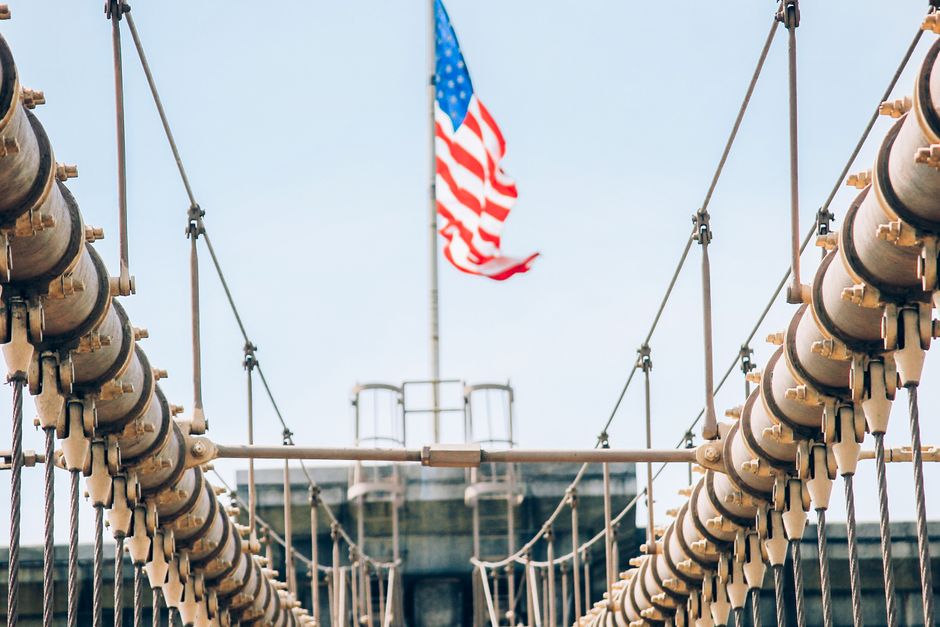 Close-up view of Brooklyn Bridge cables with an American flag waving in the background.