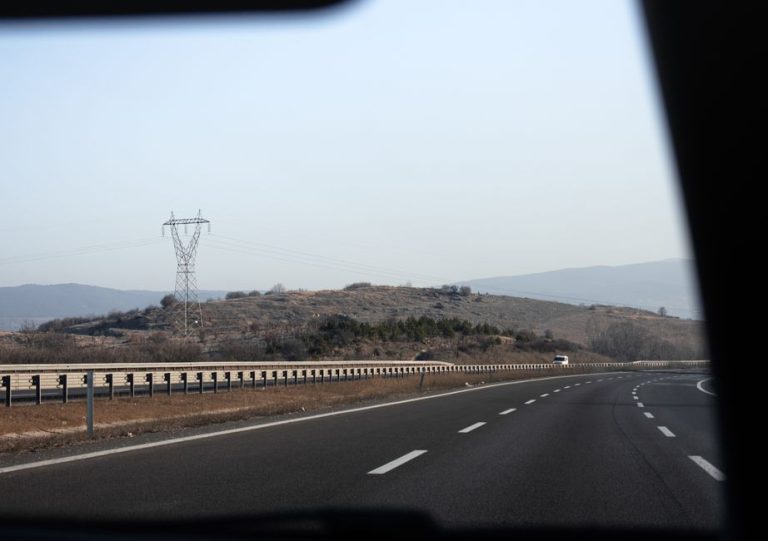 Perspective of a highway with power lines and distant hills, viewed from a car's interior.