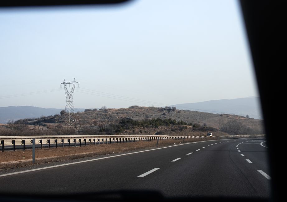 Perspective of a highway with power lines and distant hills, viewed from a car's interior.