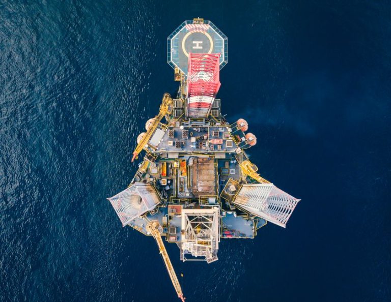 High-angle view of an offshore oil platform with helipad surrounded by deep blue ocean.