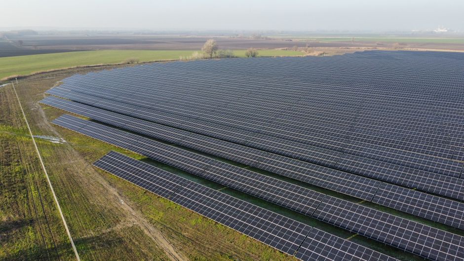 Aerial view of a vast solar panel farm in a rural landscape under clear skies.
