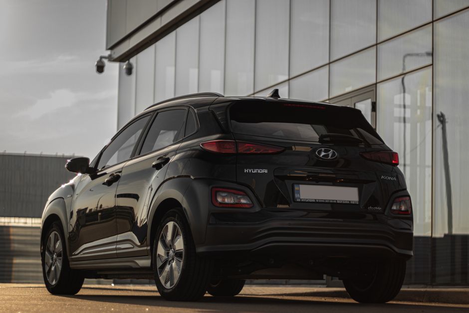 Rear view of a black Hyundai Kona parked next to a contemporary glass building reflecting urban architecture.