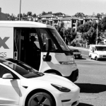 A black and white urban street scene featuring vehicles including a delivery van and a modern car.
