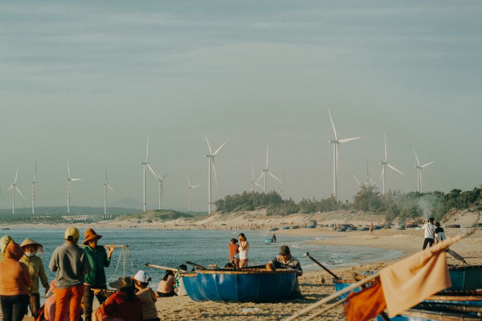 Sunny beach with wind turbines in the background, showcasing sustainable energy and local life.