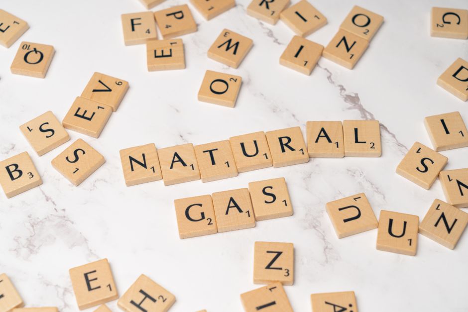 Wooden letter tiles on a marble surface spelling out 'natural gas' and scattered letters.