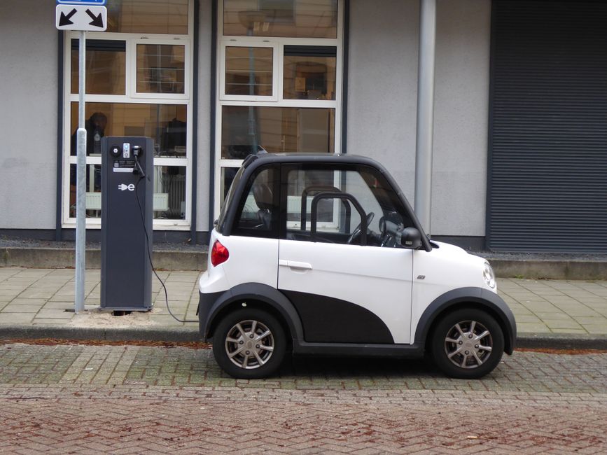 A white and black compact electric car charging at a public power station.
