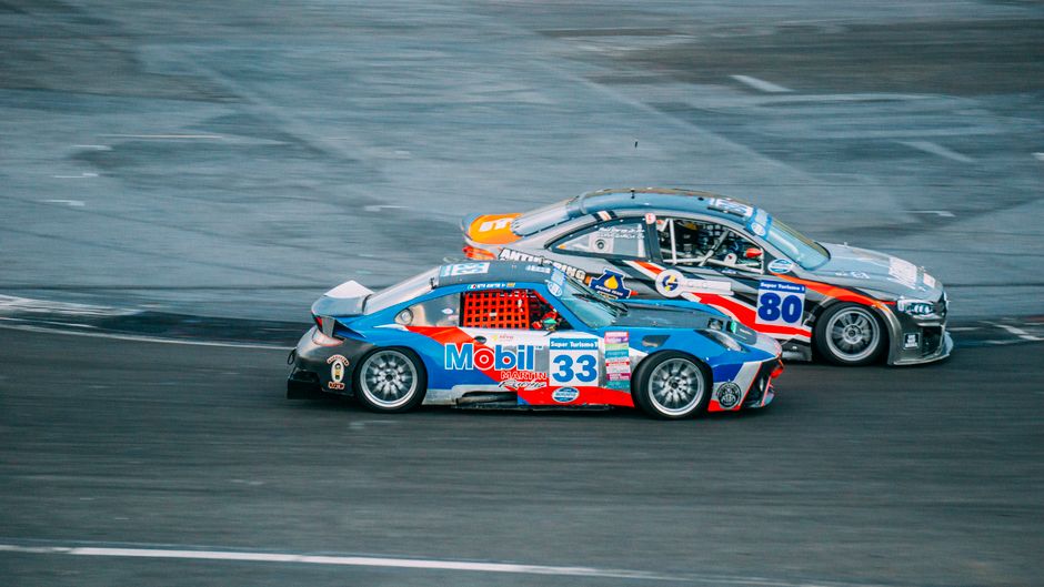 Two high-speed cars racing closely on an asphalt track during a thrilling event.