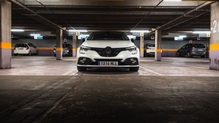 White Renault car in an underground parking garage with multiple vehicles visible.