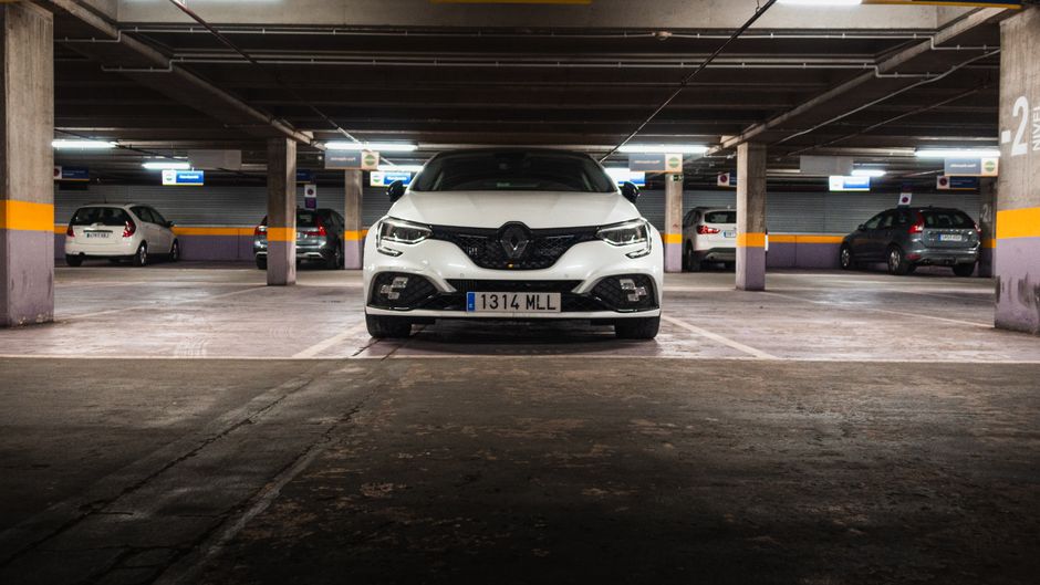 White Renault car in an underground parking garage with multiple vehicles visible.