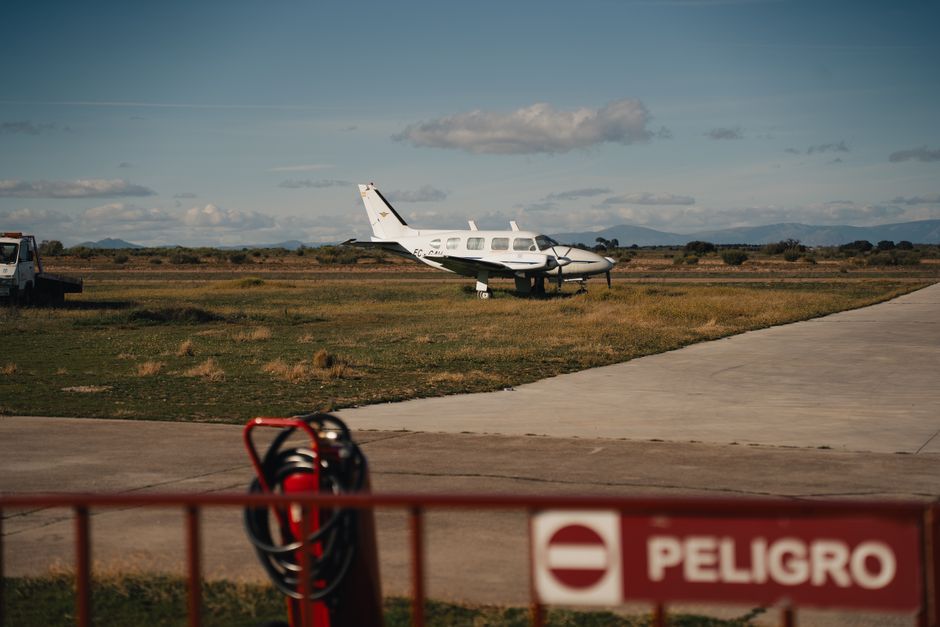 A small private aircraft parked on a grassy airfield under a clear sky with a danger sign.