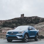 A blue Volvo electric car charging in a scenic outdoor location with a hill in the background.