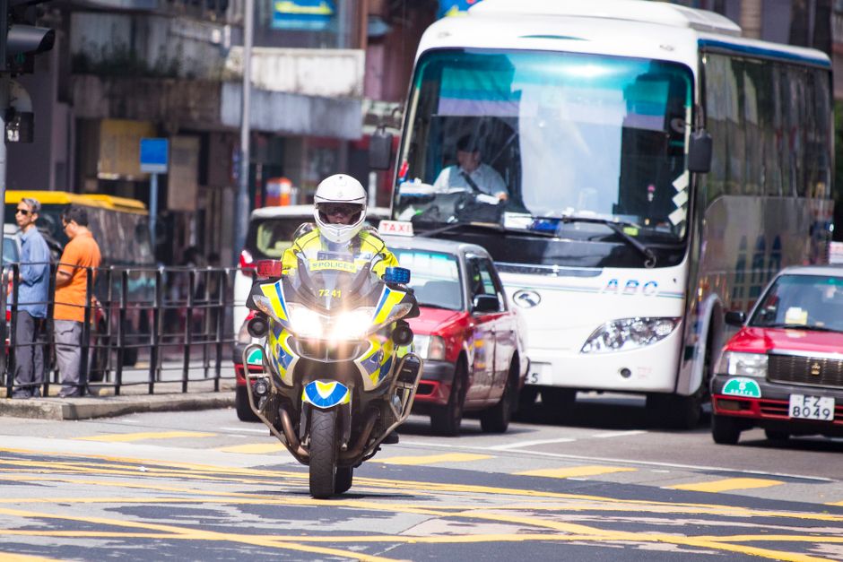 A Hong Kong police officer on a motorcycle navigating street traffic during the day.
