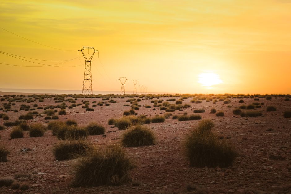 Power lines stretch across an arid desert landscape amidst a glowing sunset.