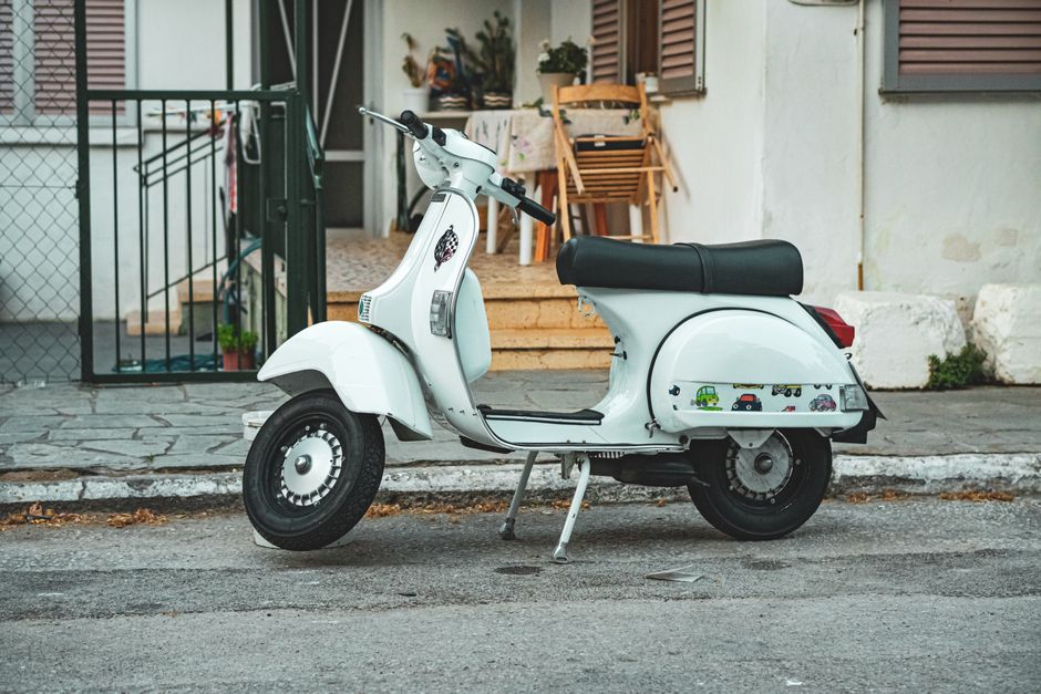 Classic white Vespa scooter parked in front of a house in Greece. Urban street scene.