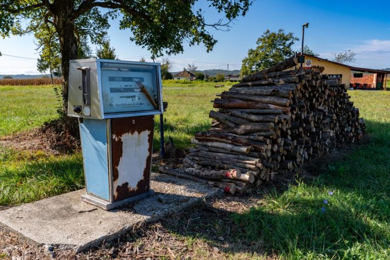 Old gas pump next to firewood stack in a sunny rural field, Garešnica, Croatia.