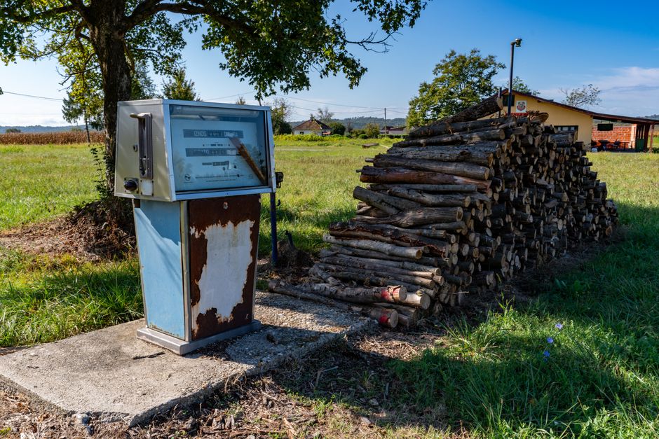 Old gas pump next to firewood stack in a sunny rural field, Garešnica, Croatia.