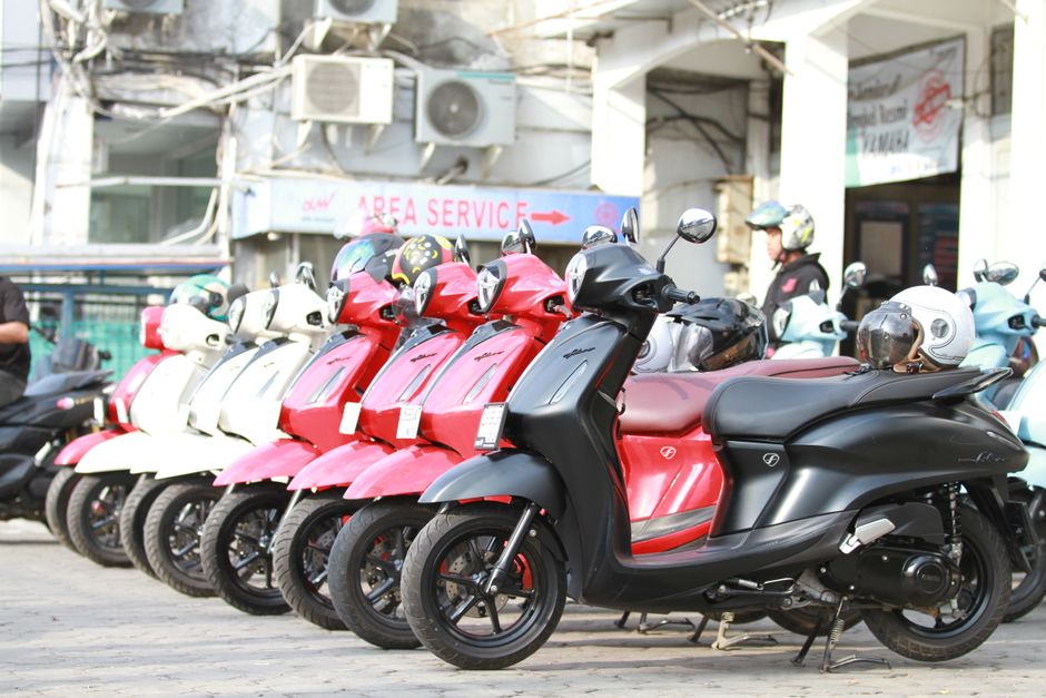 A lineup of colorful motor scooters parked outdoors at a service area, showcasing modern design.