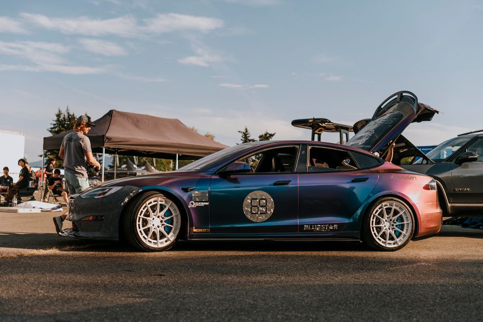 Profile view of a customized electric car at a car show under a sunny sky.