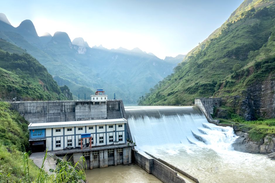 A hydroelectric dam with water flowing against a scenic mountainous backdrop.