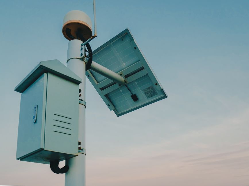 A solar panel paired with a security camera against a clear sky, representing renewable technology.