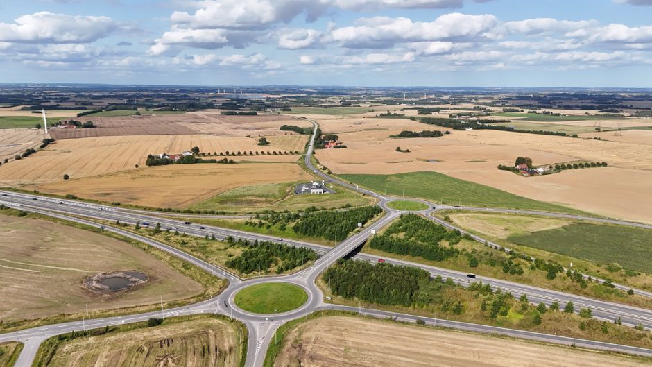 Stunning aerial view of a Danish countryside with fields and roundabout under a sunny sky.