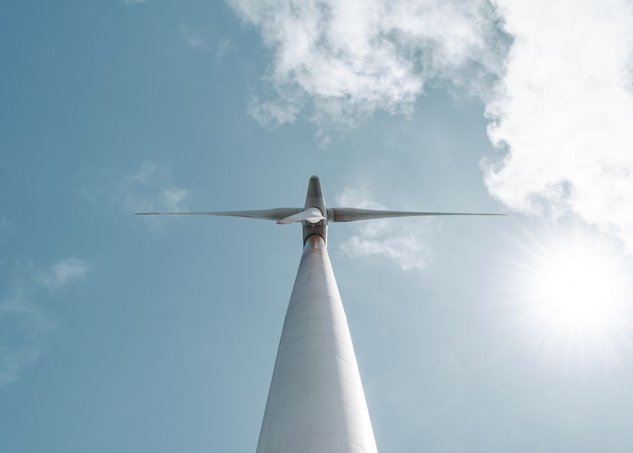 A striking view of a wind turbine from below, set against a vibrant sky with sun and clouds.