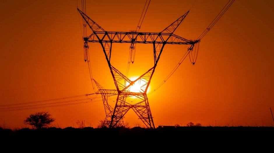 A striking sunset with electric power lines silhouetted against an orange sky in a vast open field.