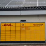 Yellow DHL Packstation under solar panels in Berlin, Germany, showcasing sustainable technology.