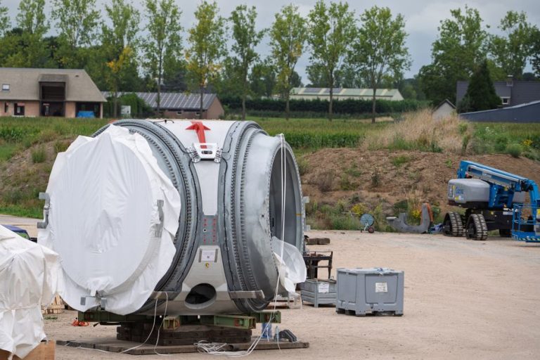 Wind turbine component at a construction site, surrounded by equipment and rural landscape.