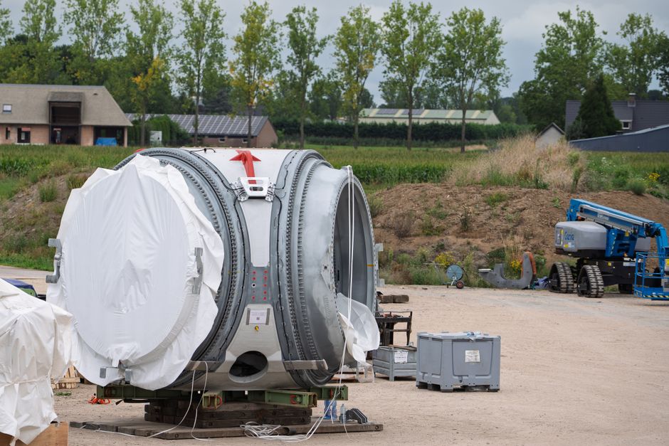 Wind turbine component at a construction site, surrounded by equipment and rural landscape.