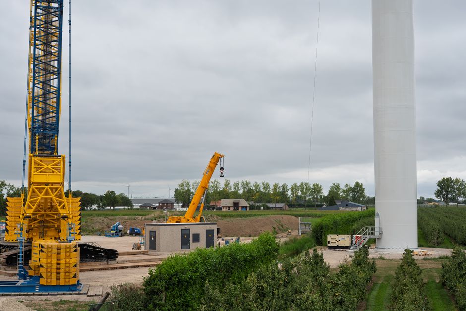 A construction site featuring cranes and a large wind turbine, set in a rural landscape.