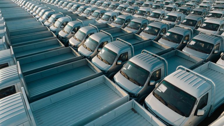 Aerial shot of multiple silver pickup trucks aligned in rows, showcasing symmetry and industrial production.