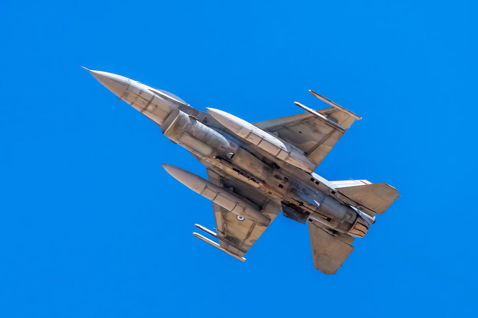 F-16 military jet flying under clear blue skies, showcasing maneuverability and power.