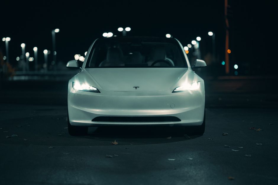 White electric car captured at night with glowing headlights, creating a moody urban feel.