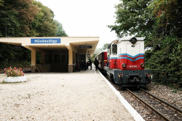 Vintage train at Hűvösvölgy station, Budapest, surrounded by lush greenery. A classic travel scene.