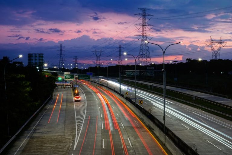Vibrant light trails on Jakarta's toll road during dusk, showcasing urban movement and a colorful sky.