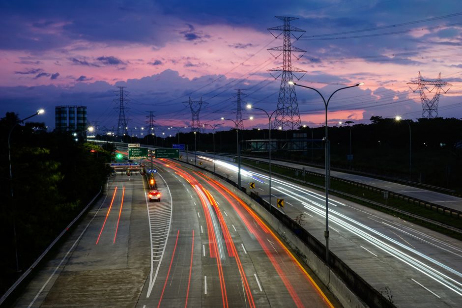 Vibrant light trails on Jakarta's toll road during dusk, showcasing urban movement and a colorful sky.